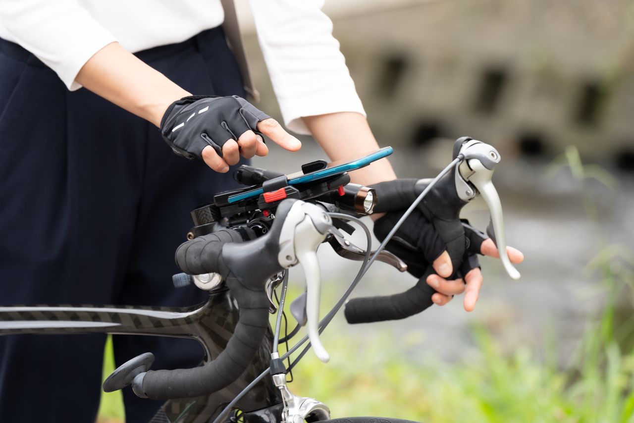 Using a smartphone while cycling, even if the device is in a holder, could lead to a steep fine. (© Pixta)