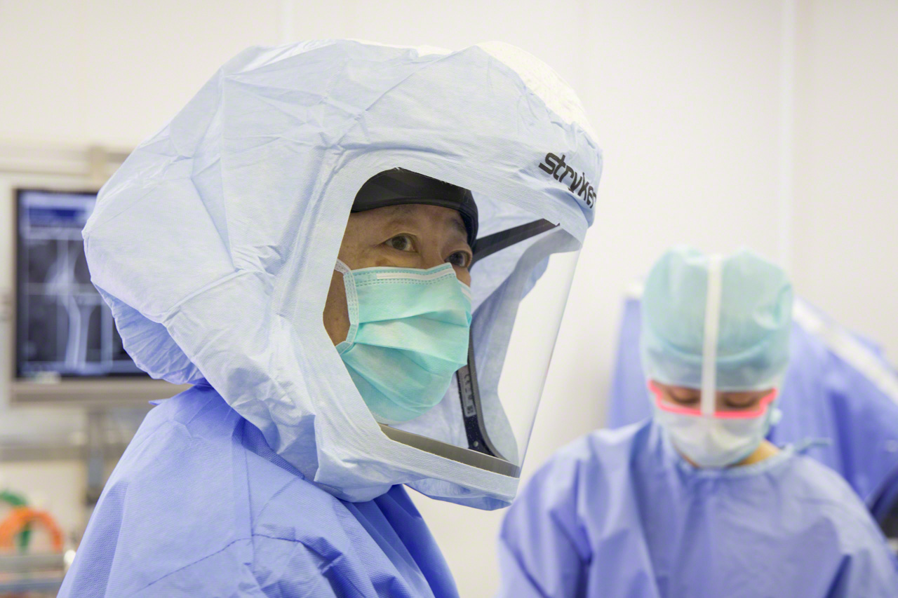 An extra layer of personal protective equipment, including a surgical helmet, is used to guard against infection, a major concern when implants are used. Matsubara jokes that he became an orthopedic surgeon so that he could dress up in a space suit. (© Ōnishi Naruaki)