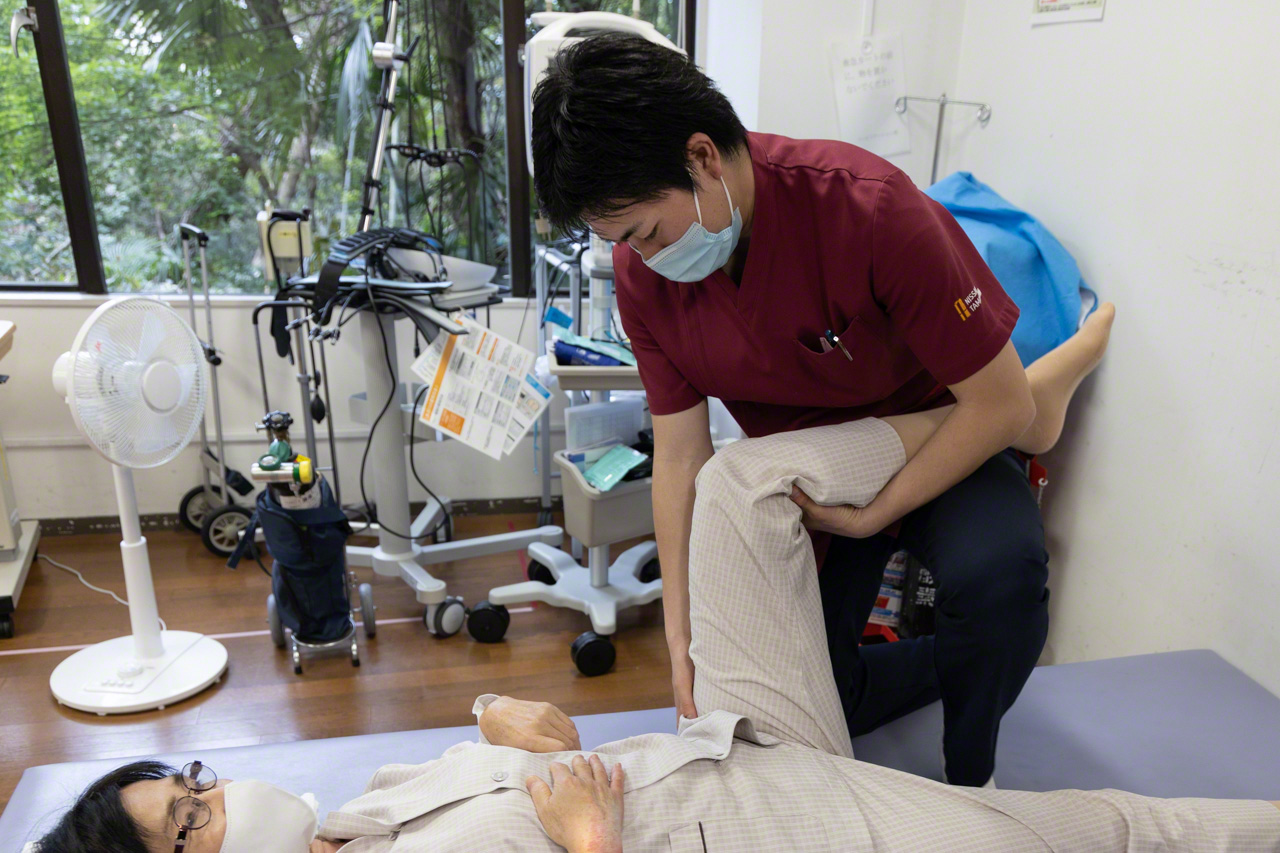 Rehabilitation begins the day after the operation. “What patients need following this surgery is not rest but movement,” says the physical therapist, shown guiding my wife through range-of-motion exercises. (© Ōnishi Naruaki)