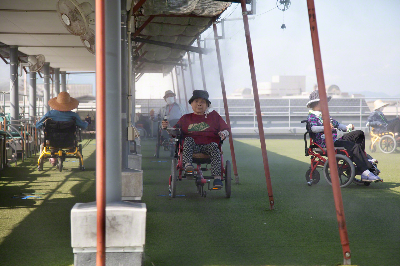 Patients take part in physical therapy on the facility’s spacious roof. “I come here because pedaling is fun,” says one. A cooling mist keeps the roof comfortable on hot days. (© Ōnishi Naruaki)