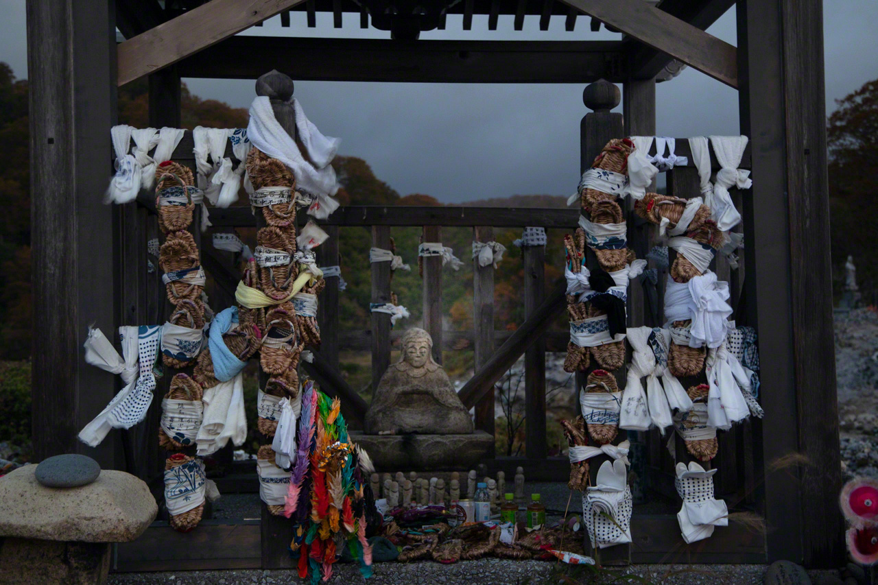 Hand towels and straw sandals surround the stone image of the Tendai priest Ennin, said to have discovered Osorezan and founded Bodaiji in 862. Pilgrims offer up the objects as prayers to speed the souls of the dead on their journey to the afterworld. (© Ōnishi Naruaki)