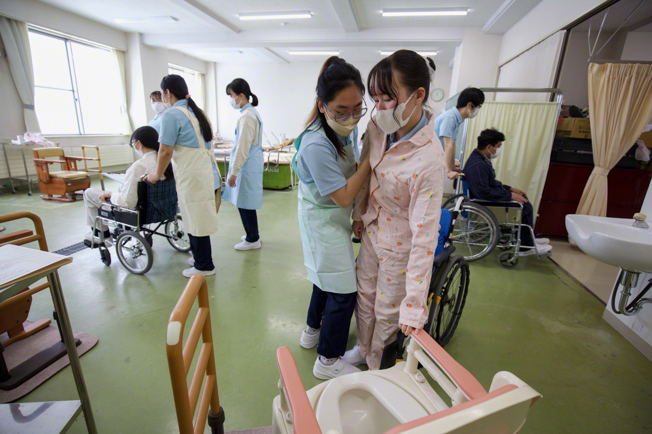 Students practice helping people move from their wheelchairs. (© Ōnishi Naruaki)
