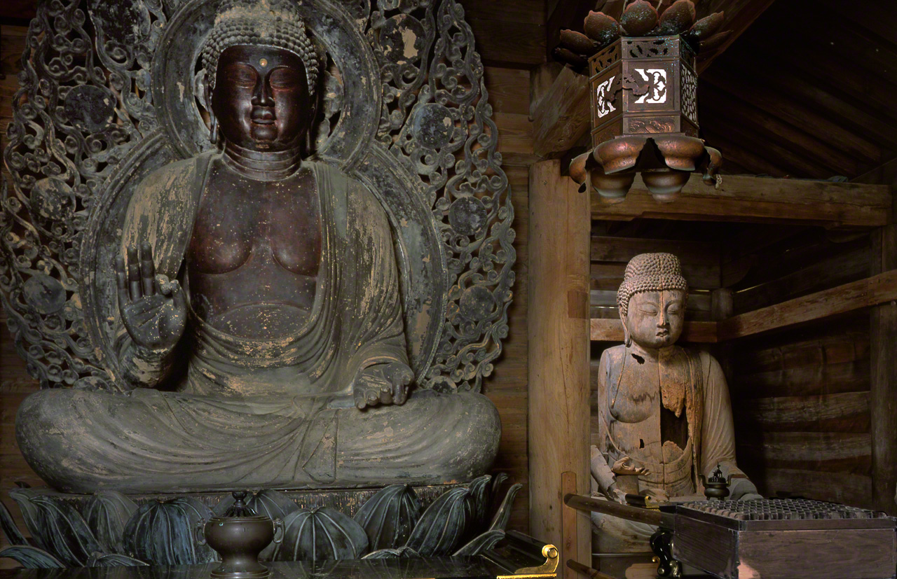 Two seated sculptures of Amida: the main image (on the left) with the damaged “old image” in the background (© Muda Tomohiro)