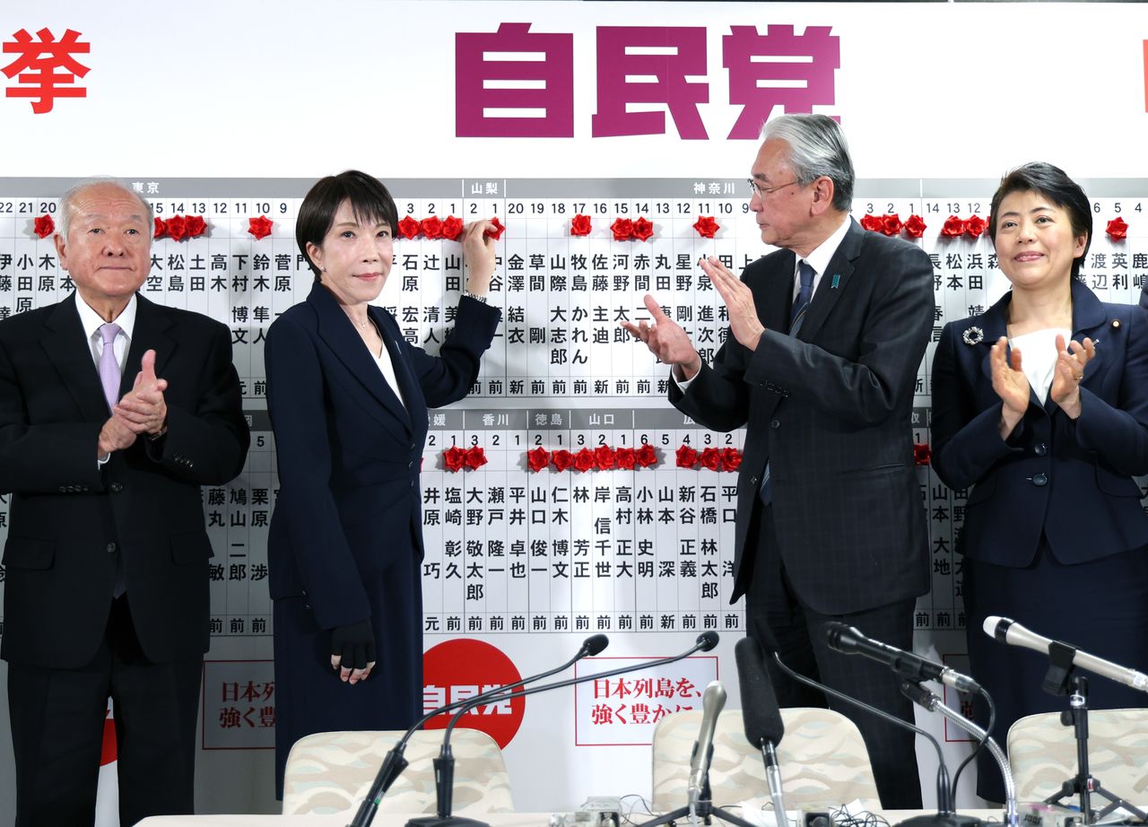 Prime Minister Takaichi Sanae, second from left, affixes flowers to the names of winning candidates from her party at LDP headquarters in Chiyoda, Tokyo, on the night of February 8, 2026. (© Jiji)