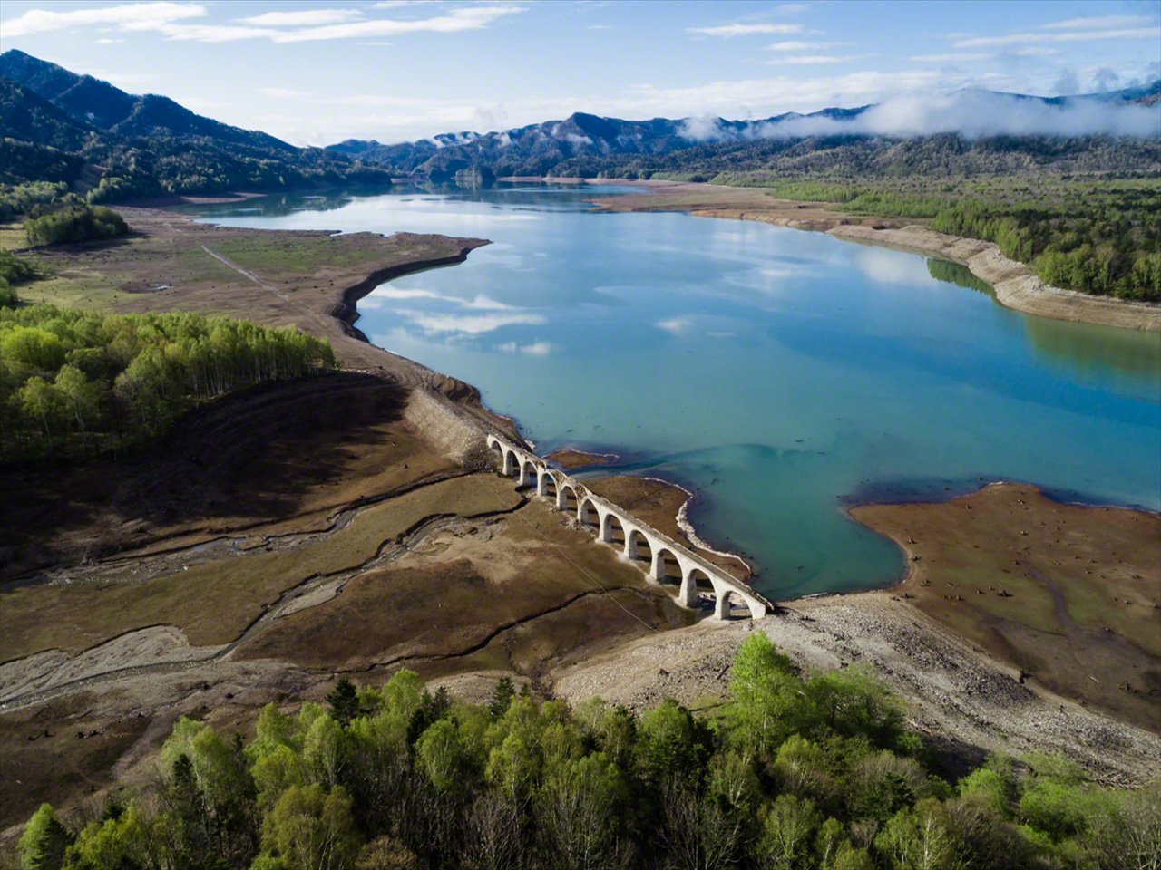 En mayo el paisaje se cubre de verde. La nieve derretida fluye hasta el lago y la superficie del agua se acerca a la base del puente.