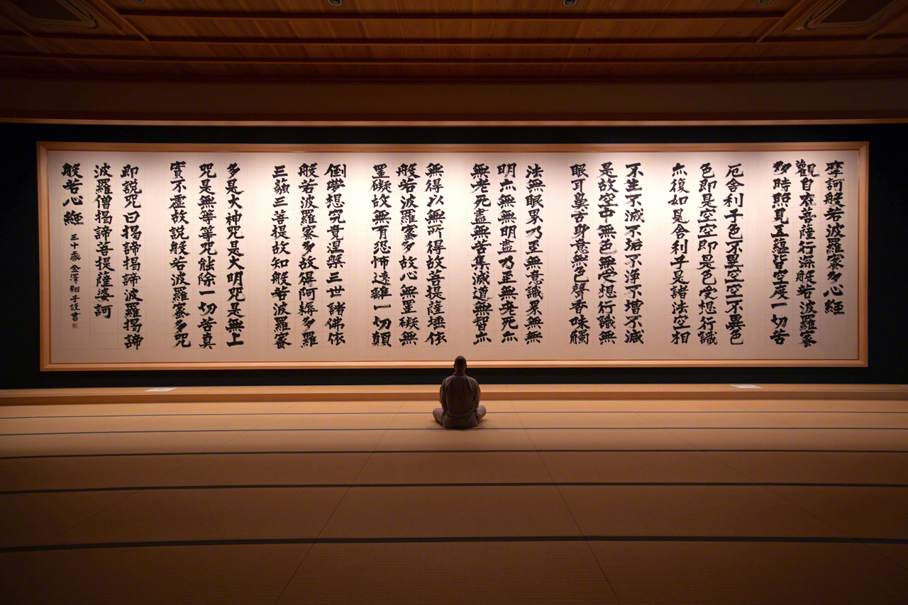 Le prêtre principal du Ryôun-ji, Kimiya Kôshi, assis devant le Sutra du cœur, par la calligraphe Kanazawa Shôko, atteinte du syndrome de Down. 