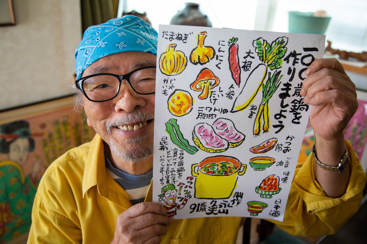 Нагаяма демонстрирует свою работу – талантливо выполненную красочную схему приготовления хякусай набэ, тушеного блюда, включающего в себя множество продуктов, способствующих долголетию (© Ониси Наруаки)